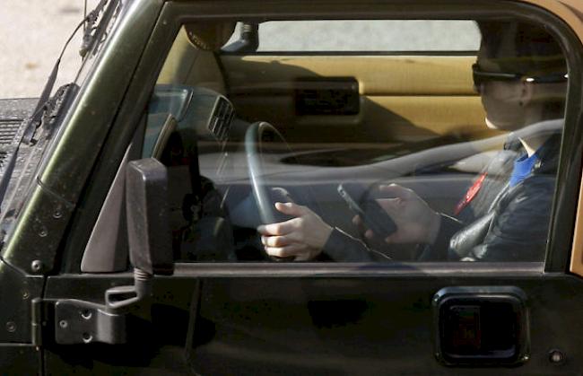 Ein Autolenker bedient sein Smartphone während der Fahrt (Archiv)