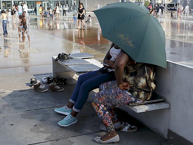 Fast 40 Grad in Genf: Auf der Place des Nations schützen sich die einen mit einem Schirm vor der Sonne, und die anderen geniessen das Wasserspiel.
