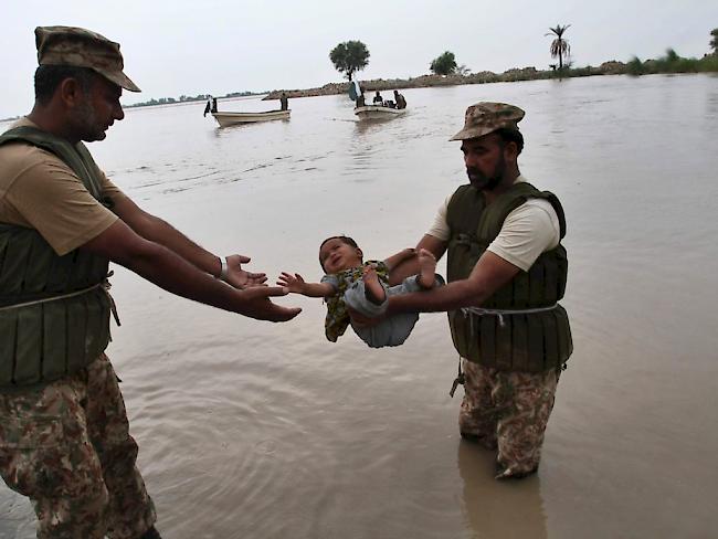 Pakistanische Rettungskräfte bringen ein Kleinkind aus einem überschwemmten Gebiet in Sicherheit.
