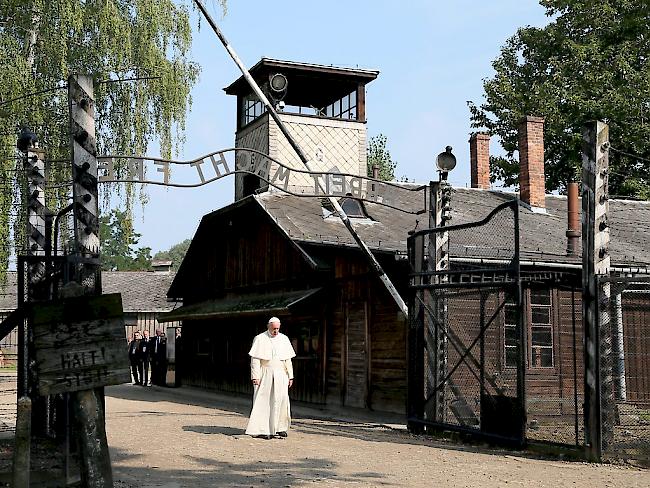 Papst Franziskus durchschreitet mit ernster Miene das Eingangstor des früheren Stammlagers Auschwitz, über dem der zynische Spruch "Arbeit macht frei" steht.