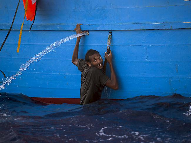 Ein Mann klammer sich an ein Boot im Meer vor Libyen, wo die italienische Küstenwache rund 6500 Flüchtlinge aus Seenot rettete.