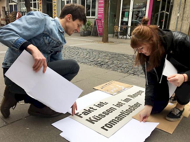 Kommunikationsdesign-Studenten legen in der Innenstadt von Mainz eine Schablone auf den Boden. Das Spray für die Aktion wird nur bei Kontakt mit Nässe sichtbar, also zum Beispiel wenn es regnet.