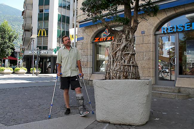 Gemeindegärtner Ueli Jordi mit lädiertem Fuss neben dem Riesenbaum-Bonsai an der Visper Bahnhofstrasse.