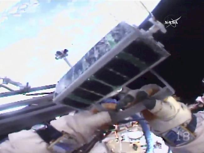 Der russische Kosmonaut Sergei Ryazansky setzt bei der internationalen Raumstation ISS einen Minisatelliten von Hand im Weltall aus.