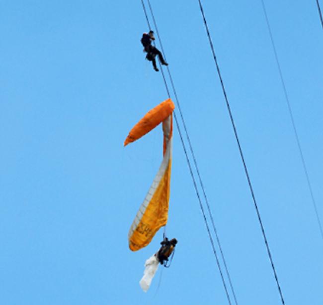 Der unverletzte Gleitschirmpilot in seiner misslichen Lage. Ein Rettungsspezialist der Air Zermatt eilt zu Hilfe.