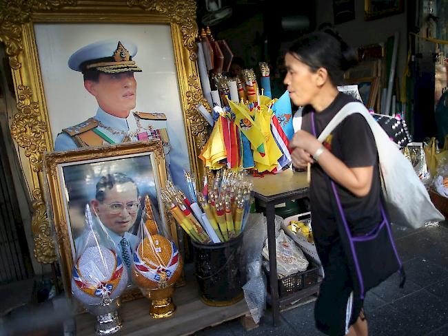 Ein Frau läuft in der thailändischen Hauptstadt Bangkok an den Porträts des verstorbenen Königs Bhumibol Adulyadej (unten) und des Kronprinzen Maha Vajiralongkorn (oben) vorbei. Letzterer will die Nachfolge seines Vaters frühestens in einem Jahr antreten.