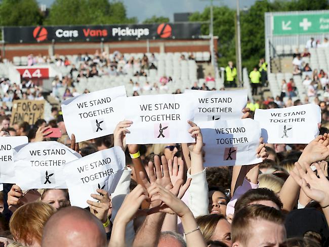 Besucher des Benefiz-Konzerts halten Schilder mit der Aufschrift "Wir stehen zusammen" hoch.