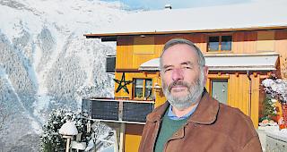 Ruedi Lehmann vor einem Haus in Bellwald, mit im Balkongel&auml;nder integrierten Photovoltaikpanels.