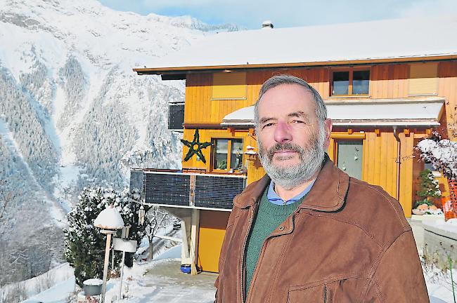 Ruedi Lehmann vor einem Haus in Bellwald, mit im Balkongeländer integrierten Photovoltaikpanels.