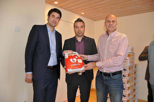 Dr. Aron Pfammatter von coeur wallis (links) und Diego Lareida von der Kantonalen Walliser Rettungsorganisation (rechts) übergeben dem Gemeindepräsident von Veyras, Stéphane Ganzer, einen Defibrillator.