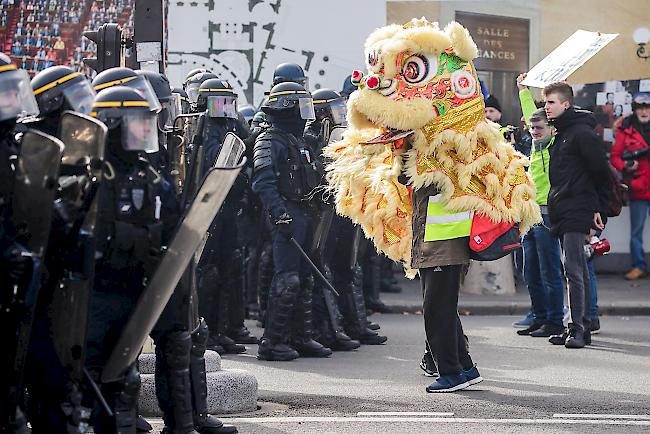 Ein als chinesischer Neujahrsdrache kostümierter Demonstrant steht vor einer Reihe von Sicherheitskräften.