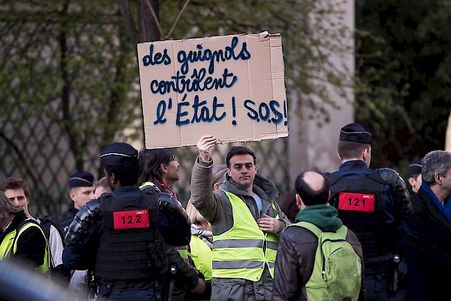 Ein «Gelbwesten»-Demonstrant hält ein Plakat mit der Aufschrift «Guignols (Dummköpfe) regieren Frankreich! SOS!».