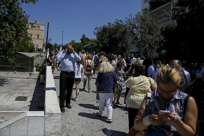 Nach einem starken Erdbeben am Freitag in der Nähe der griechischen Hauptstadt Athen telefonieren die Leute vor dem Gebäude, in dem sie arbeiten.
