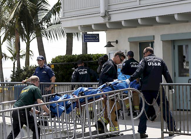 Such- und Rettungsleute transportieren zusammen mit Offizieren des Santa Barbara Sheriffs eine geborgene Leiche auf dem Dock im Hafen von Santa Barbara.