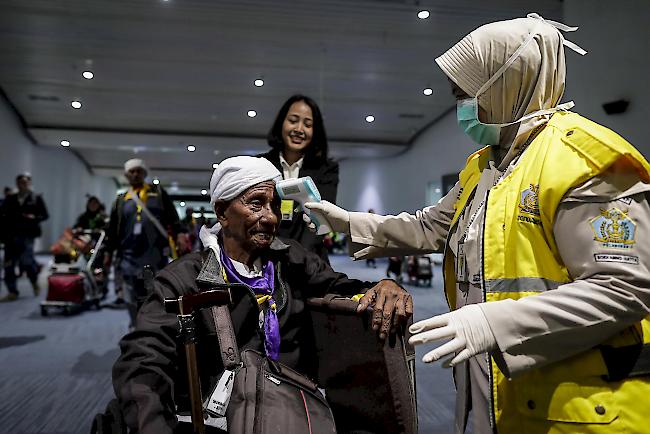 Ein indonesischer Quarantänebeamter misst die Temperatur eines Passagiers bei seiner Ankunft am Flughafen.