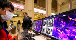 Ein Mitarbeiter von Malaysia Health &uuml;berpr&uuml;ft am Flughafen Kuala Lumpur Passagiere, die einen W&auml;rmescanner durchlaufen.